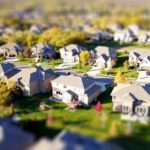 Tilt-shift aerial photo of a suburban neighborhood with green lawns and roads.