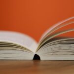 An open book with pages turning against a vibrant orange background, symbolizing knowledge and education.