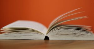 An open book with pages turning against a vibrant orange background, symbolizing knowledge and education.