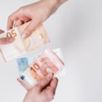 Close-up of hands exchanging euro bills, symbolizing finance and transaction.