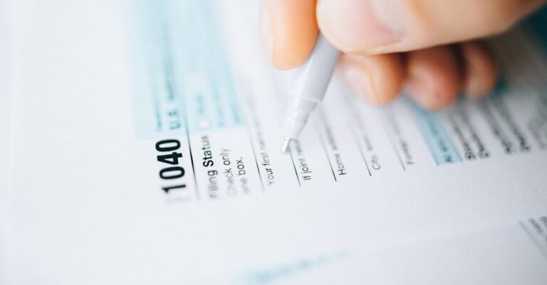 Close-up of a hand using a pen to fill out a tax form 1040, focusing on details.
