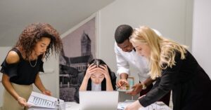 Diverse group of coworkers engaged in a collaborative office meeting, discussing around a laptop.